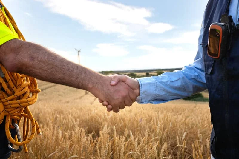 Dos personas dándose la mano en un campo agrícola como símbolo de acuerdo comercial o cierre de trato