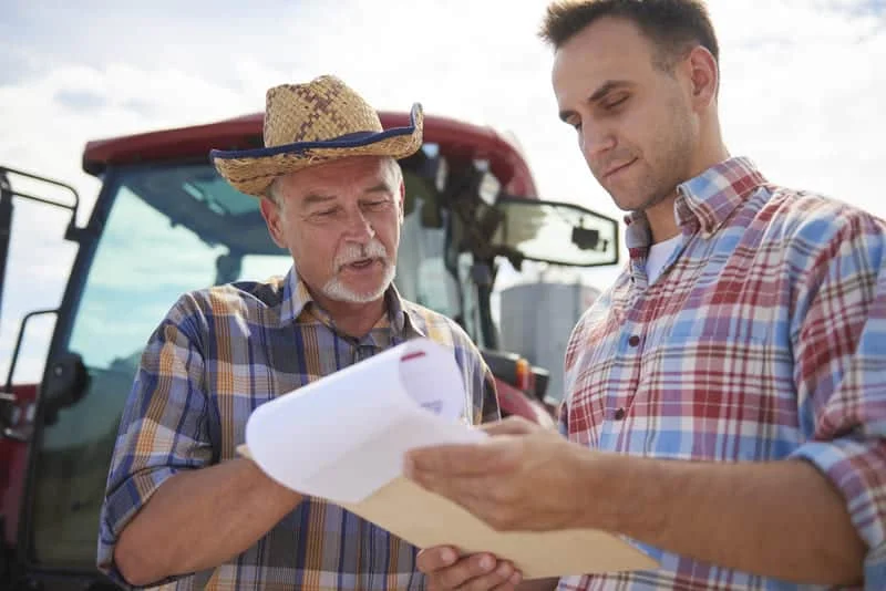 Dos hombres revisando y discutiendo cotizaciones de tractores agrícolas durante una reunión comercial