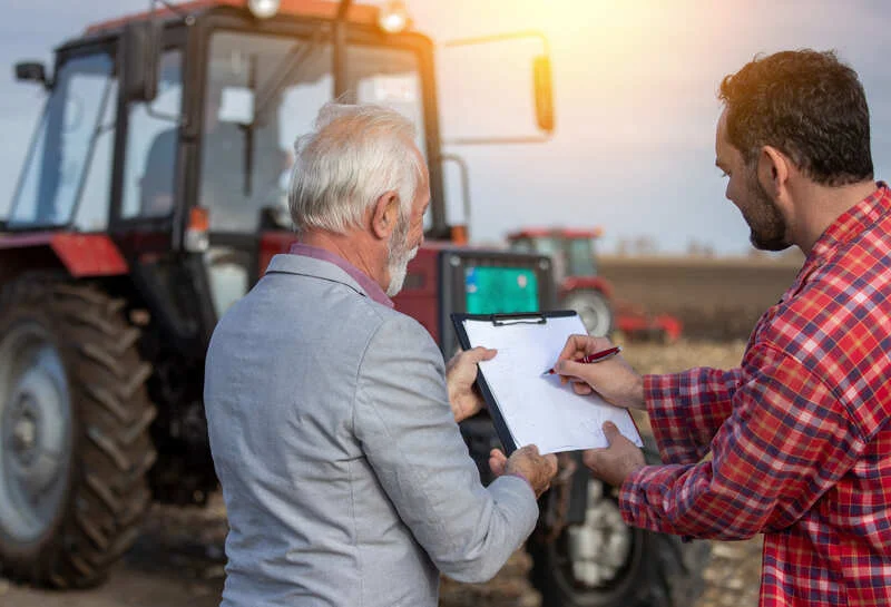 Dos hombres conversando antes de firmar un contrato de compra de tractor, revisando términos y condiciones