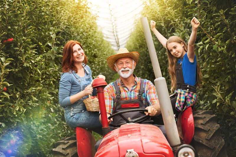 Familia sentada sobre un tractor rojo, disfrutando de un momento en el campo con maquinaria agrícola