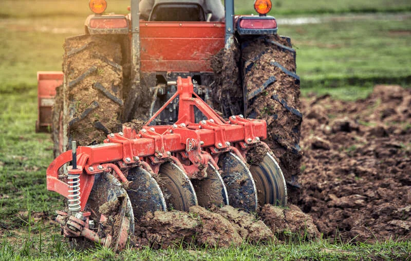 Tractor agrícola arando el campo con implemento de arado, removiendo el suelo para la próxima siembra