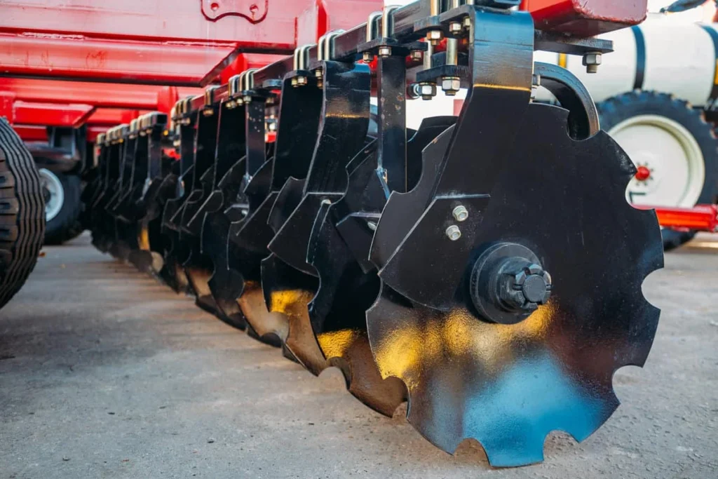 Rastra de discos roja en campo agrícola, implemento conectado a tractor para labores de preparación del suelo