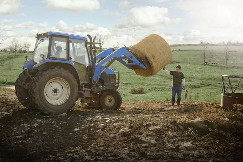 Tractor agrícola maniobrando en espacio estrecho entre cultivos o estructuras rurales