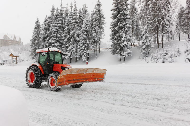 Tractor agrícola rojo equipado con pala frontal retirando nieve de un camino rural
