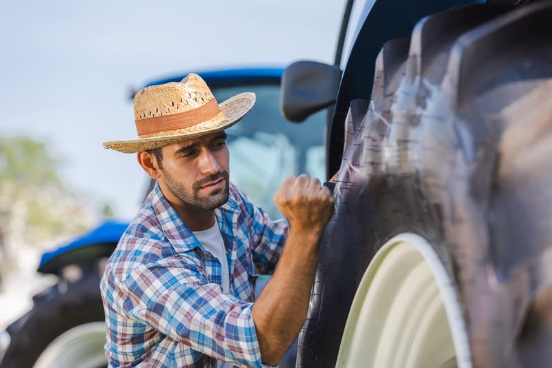 Agricultor verifica el estado de la llanta de un tractor en el campo, asegurando su buen funcionamiento.