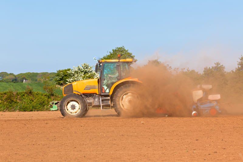 Tractor agrícola moderno trabajando en campo rural durante la cosecha bajo cielo despejado.