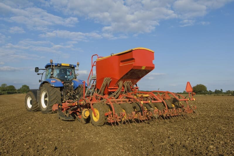Tractor moderno con implementos agrícolas trabajando en campo de cultivo durante el día.