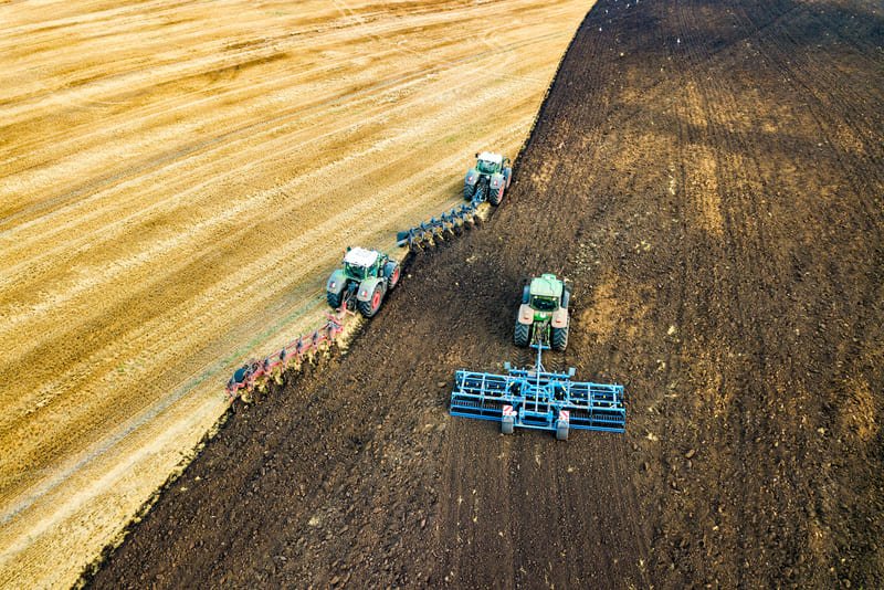 Tractor agrícola moderno con diferentes implementos trabajando en campo abierto bajo cielo despejado.