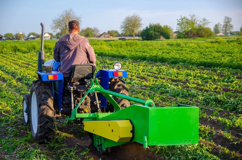 Tractor compacto equipado con cosechadora de papas trabajando en un campo agrícola latinoamericano.