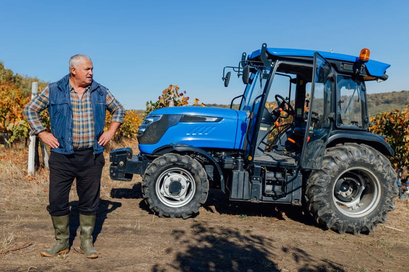 Hombre seleccionando un tractor agrícola en una granja bajo cielo azul, maquinaria agrícola moderna.