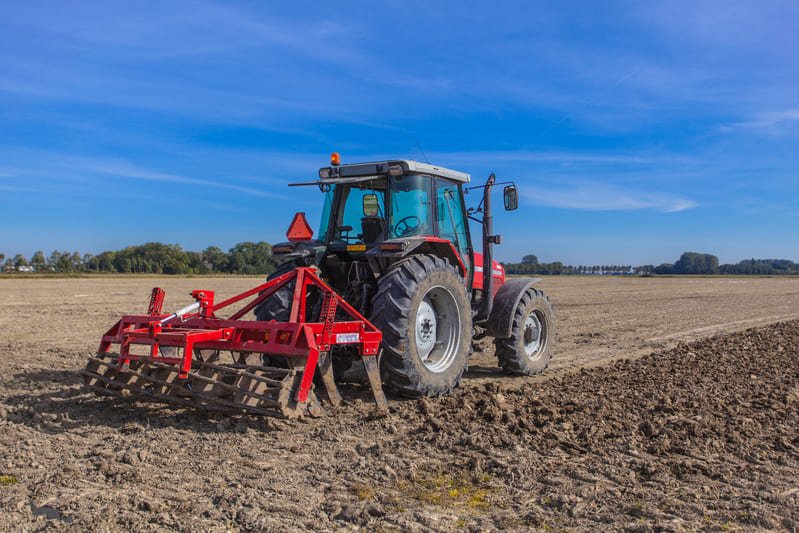 Tractor agrícola realiza compactación de suelo en campo agrícola durante labores de preparación.